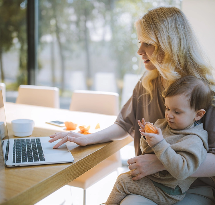 Woman looking at laptop while holding baby